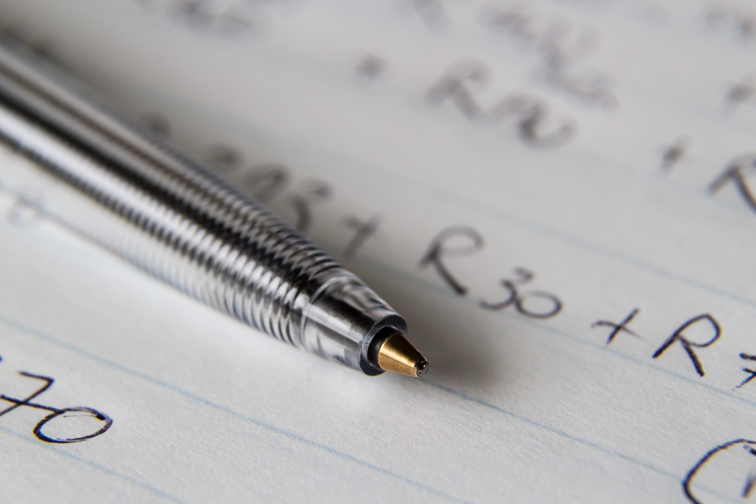 A closeup shot of a black pen on a piece of paper with some numbers and codes written on it